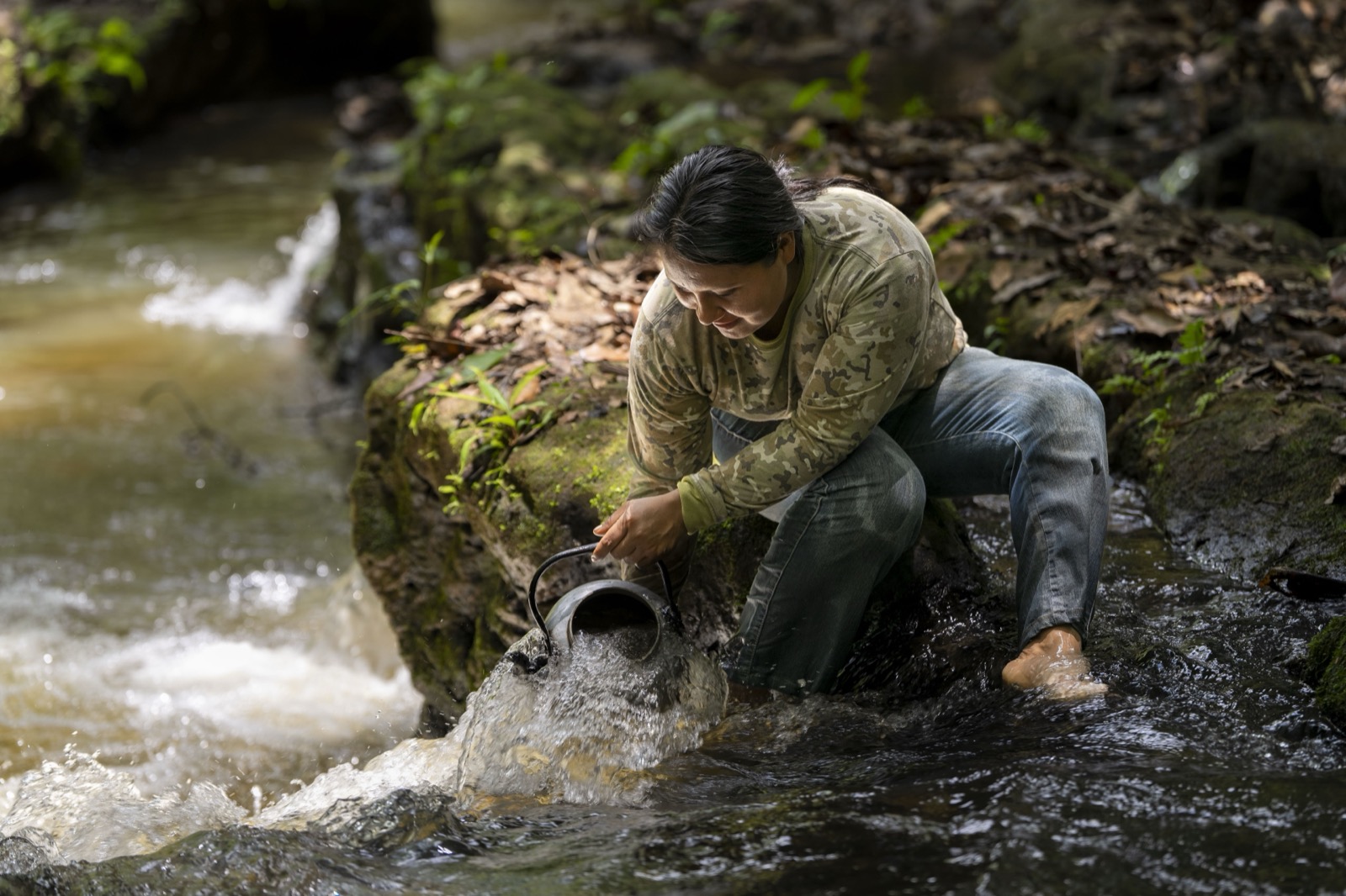 Mujer recogiendo agua del arroyo